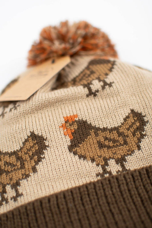 Close-up of brown hen knit pattern with rust-orange accents on an oatmeal farmhouse winter beanie made from 100% acrylic.