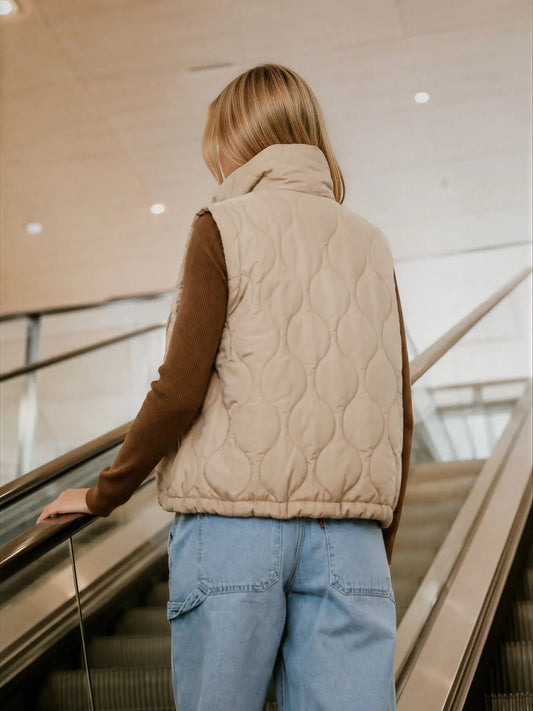 Back view of beige wave quilted women’s vest with high collar and elastic hem