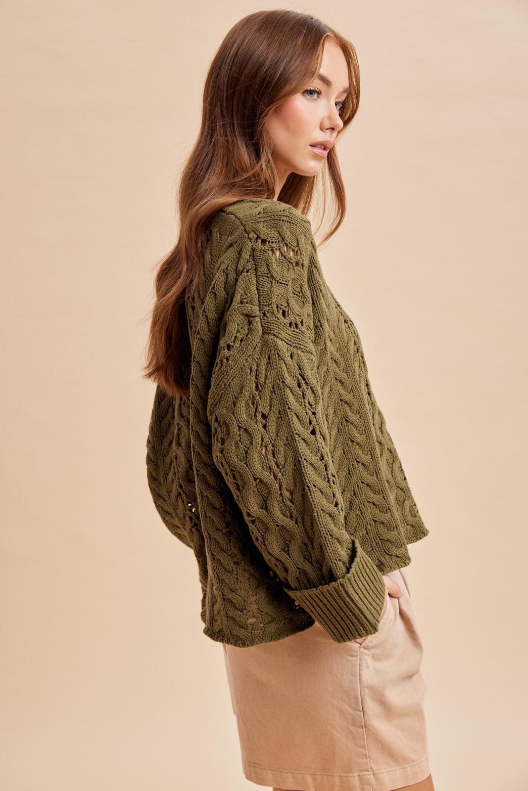 Side view of women's olive green chunky cable knit sweater with relaxed fit and cuffed sleeves
