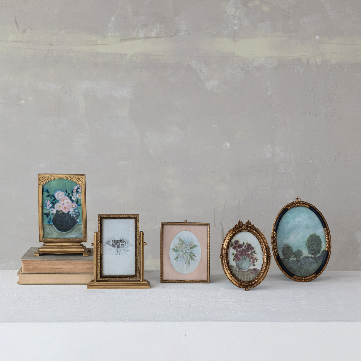 Six vintage-inspired gold pewter and glass picture frames in ornate oval and rectangular styles with artwork