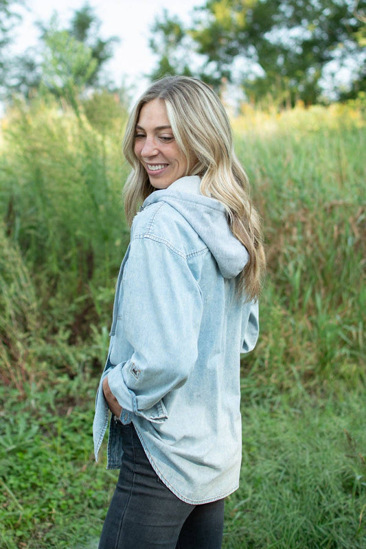 Side and back view of women's light wash denim shacket featuring a gray hood, relaxed silhouette and curved hem.