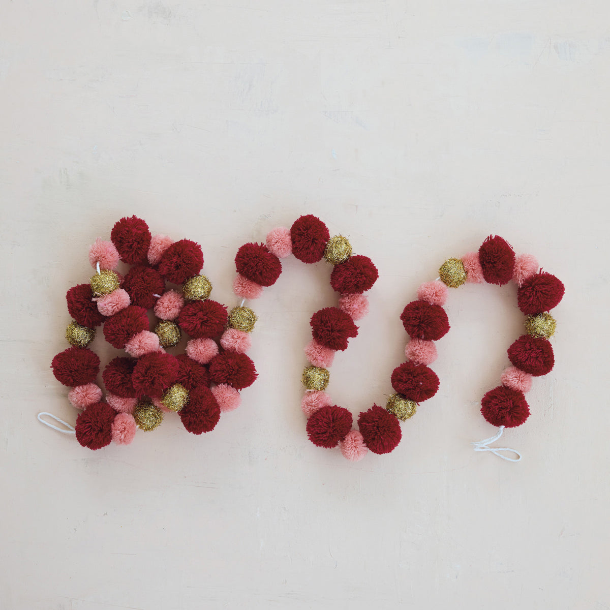 Close-up of burgundy pink and metallic gold polyester pom poms on decorative garland