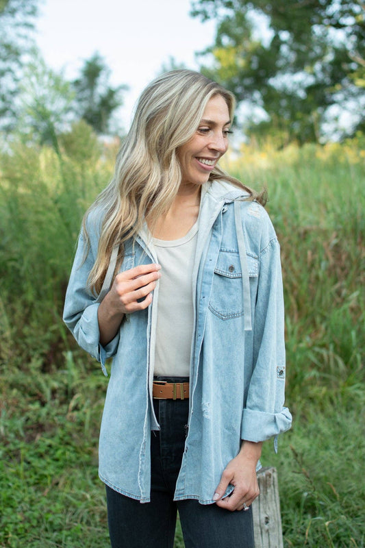 Woman wearing a light wash hooded denim shacket with gray hoodie insert, button-front styling and rolled sleeves.