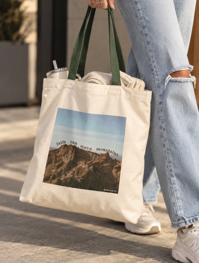 Woman carrying Faith Can Move Mountains Christian canvas tote bag with green handles
