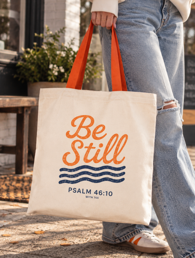 Woman carrying Be Still Psalm 46:10 Christian canvas tote bag with orange handles