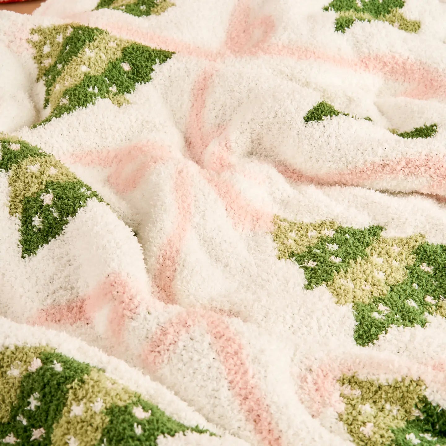 Close up of soft Christmas blanket with pink bows and green trees
