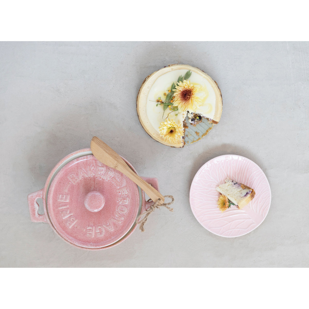 Pink stoneware brie baker with bamboo spreader styled with baked brie and serving plate