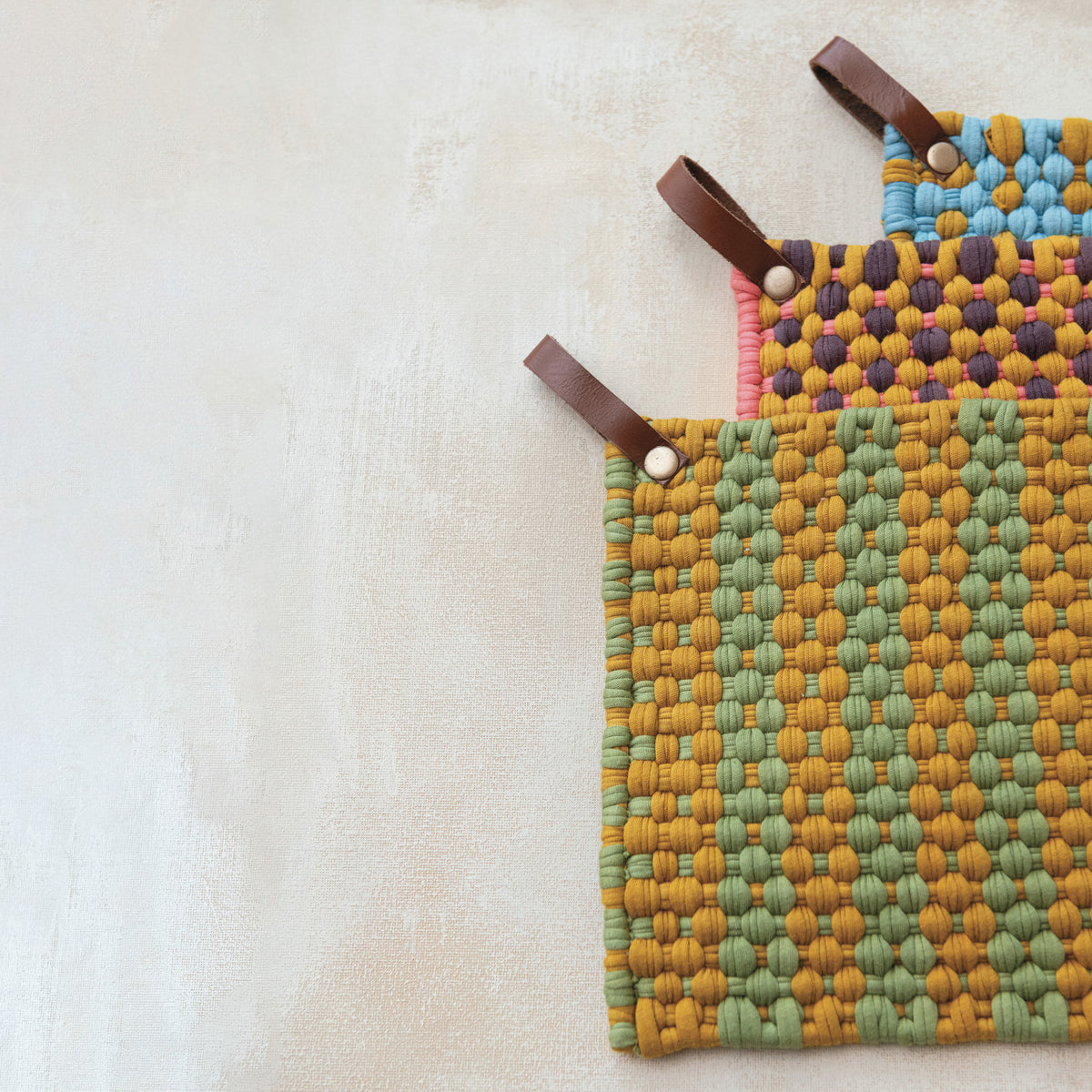 Colorful woven cotton pot holders with leather hanging loops in sage, pink and blue