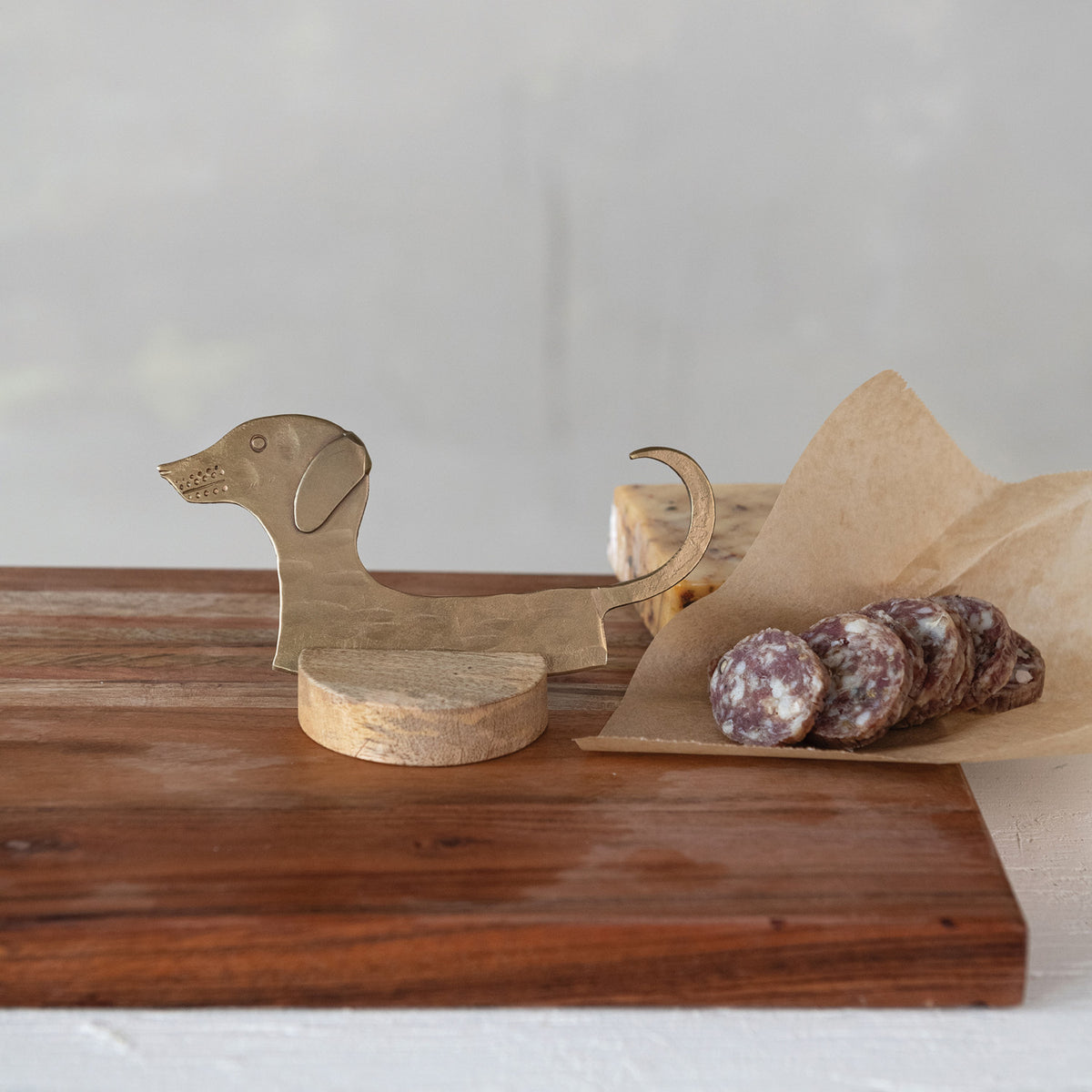 Dachshund cheese knife with mango wood stand displayed on charcuterie board with sliced salami
