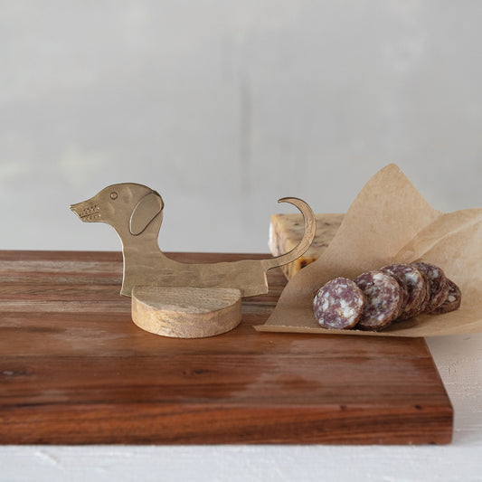 Dachshund cheese knife with mango wood stand displayed on charcuterie board with sliced salami
