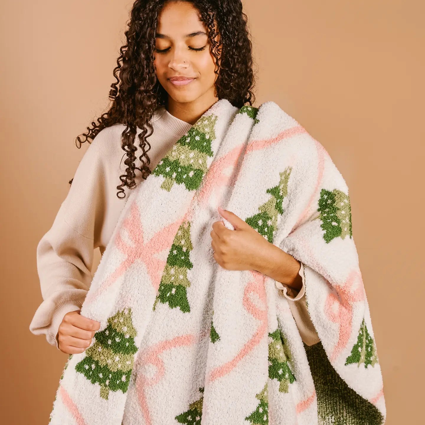 Woman wrapped in soft pink bow and green Christmas tree throw blanket