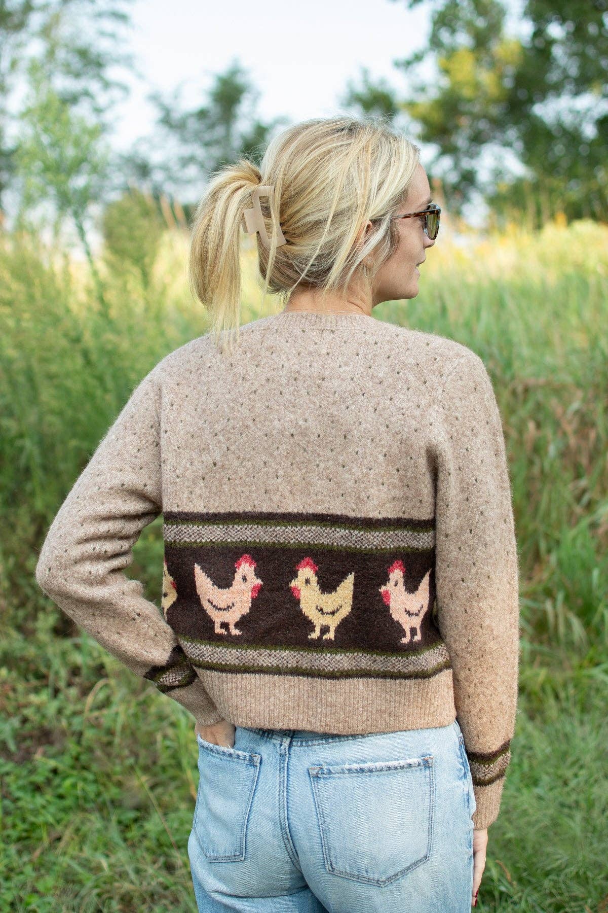 Back of women's Heritage Chicken Cardigan featuring cream chickens on brown and olive green patterned knit, paired with denim jeans.
