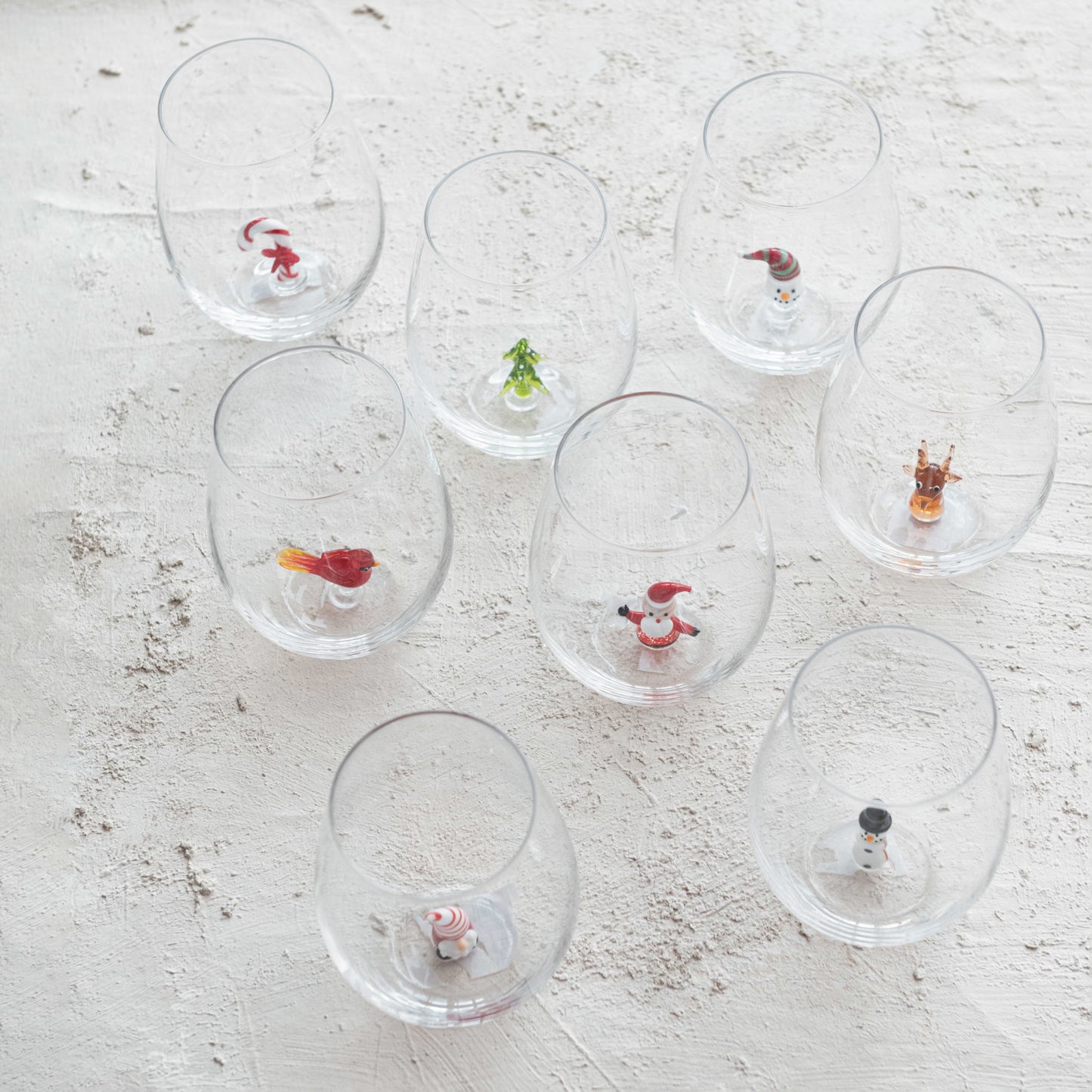 Christmas stemless wine glasses with assorted miniature holiday characters displayed on white table